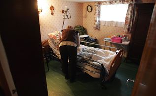En plejer står foroverbøjet over en hospitalsseng, der er placeret hjemme privat hos en borger. 