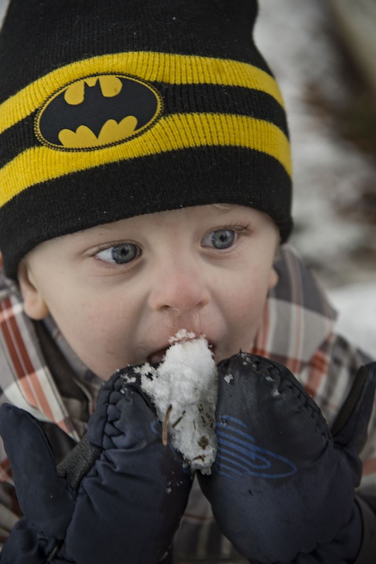 En lille dreng iført batmanhue og vintertøj spiser sne