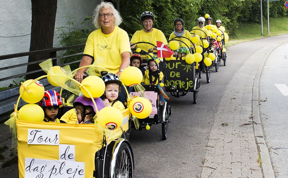 Syv voksne iført gult tøj kører på nogle christiania-cykler med børn siddende i boksen foran på cyklen