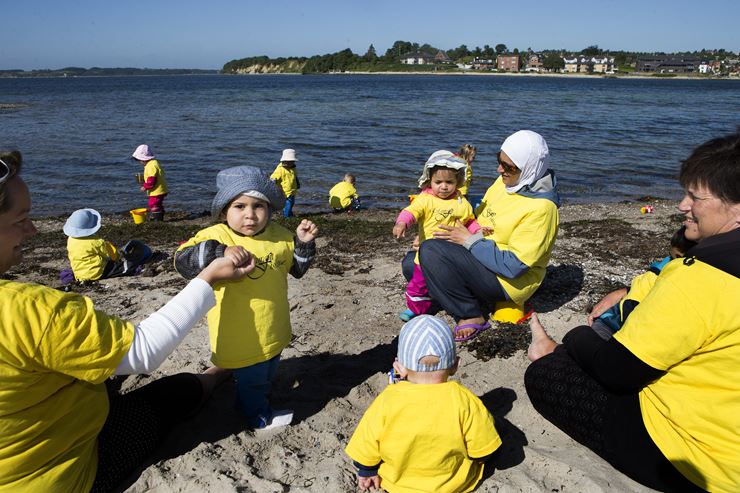 En masse voksne og børn er samlet på en strand, alle iført gule bluser