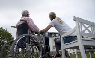 En ældre mand i kørestol taler med en yngre sosu