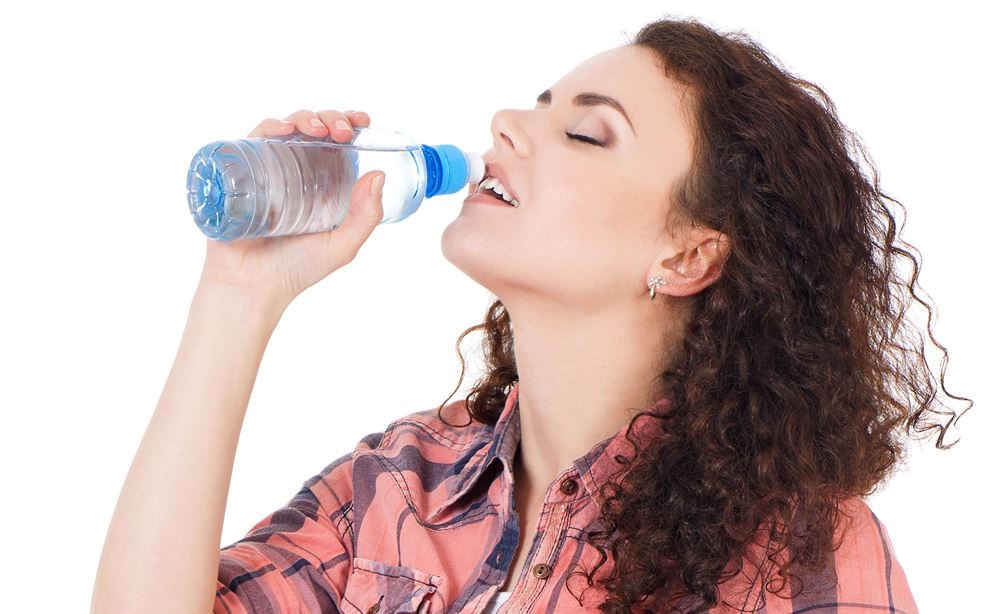 En kvinde iført ternet skjorte, drikker vand af en plasticflaske