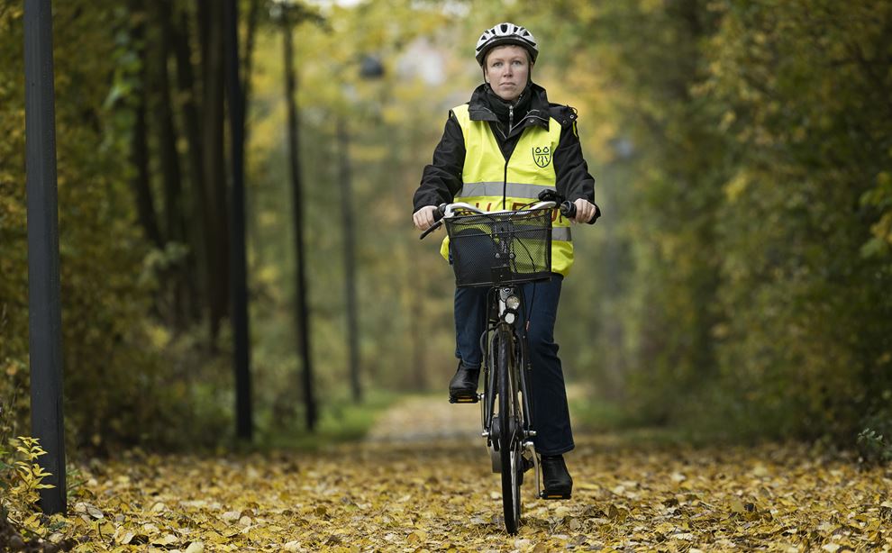 En kvinde cykler på en sti i skoven iført gul vest og cykelhjelm