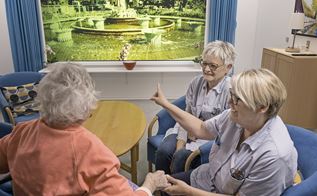 Dement kvinde ser på billeder i stimulistue med plejehjemsassistenter