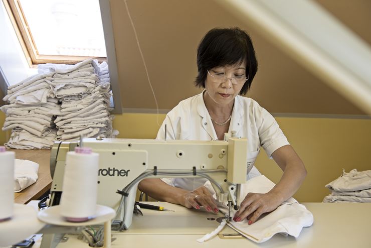 En kvinde sidder, iført hvid uniform, og syr på en symaskine