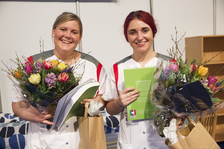 To piger står i hvid uniform med blomster og uniform i hænderne
