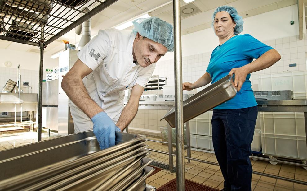 En mand og en kvinde i arbejdstøj i et storkøkken