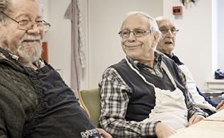 Tre mænd sidder ved et bord, den midterste sidder med et kæmpe smil på