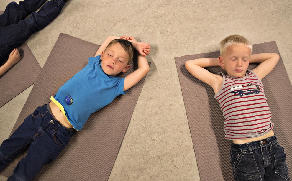To drenge ligger på gulven oven på en yoga måtte, med lukkede øjne og armene trukket op under hovedet