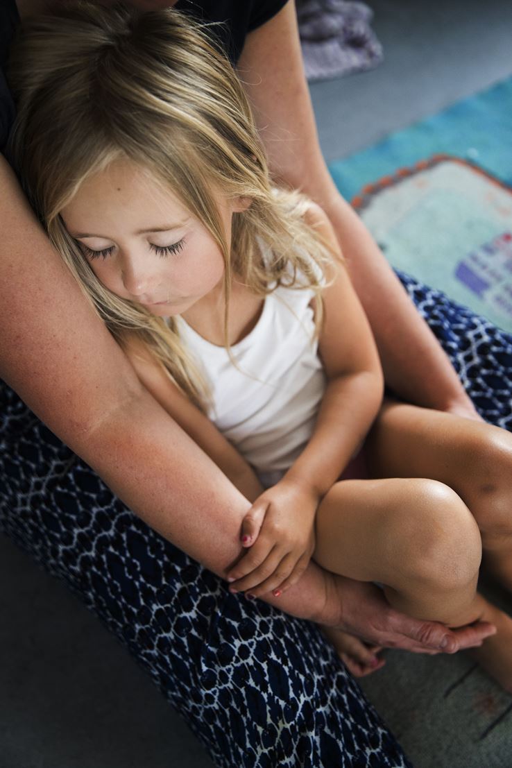 En lille lyshåret pige er faldet i søvn i armene på en voksen