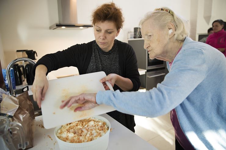 To kvinder er igang med at hælde makroner ovenpå en dessert i en hvid skål