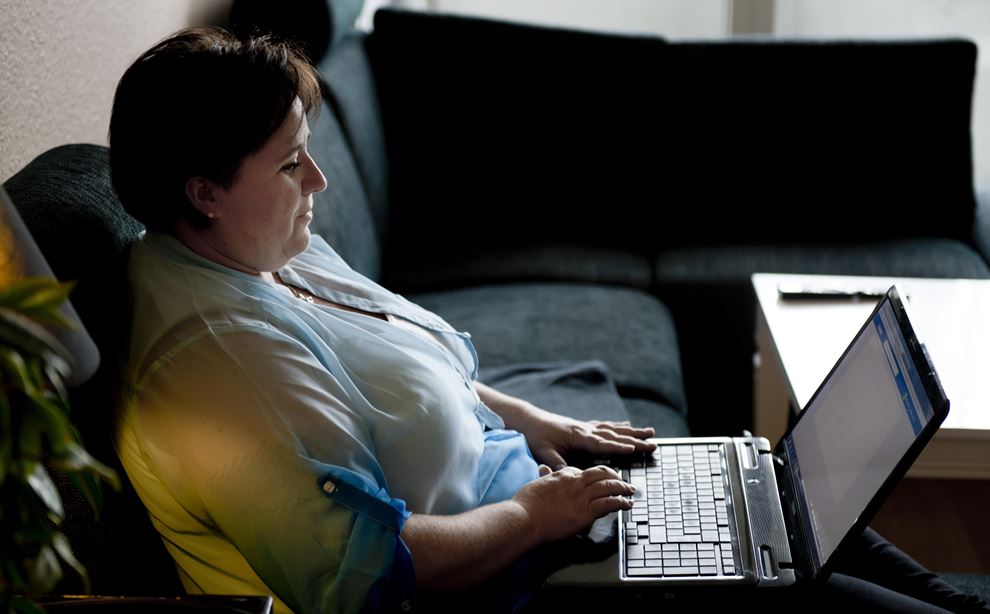 Sussie sidder i sin sofa, med en computer i skødet, og hænderne på tastaturet