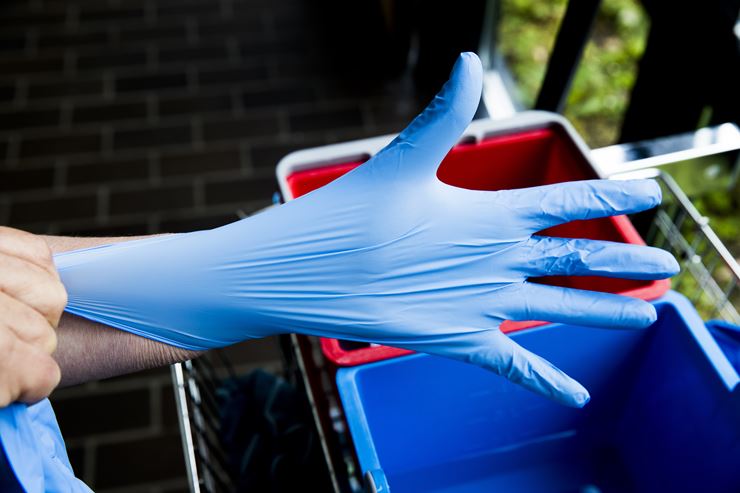 En blå plastichandske bliver trukket over en hånd. 