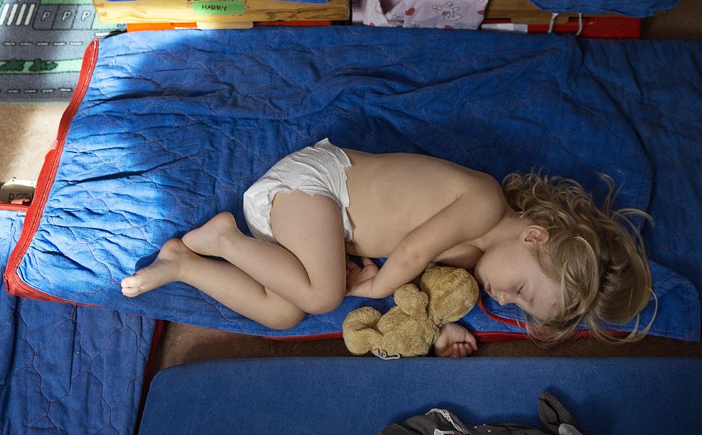 En pige ligger og sover på et blåt underlag i en sovesal - kun iført ble