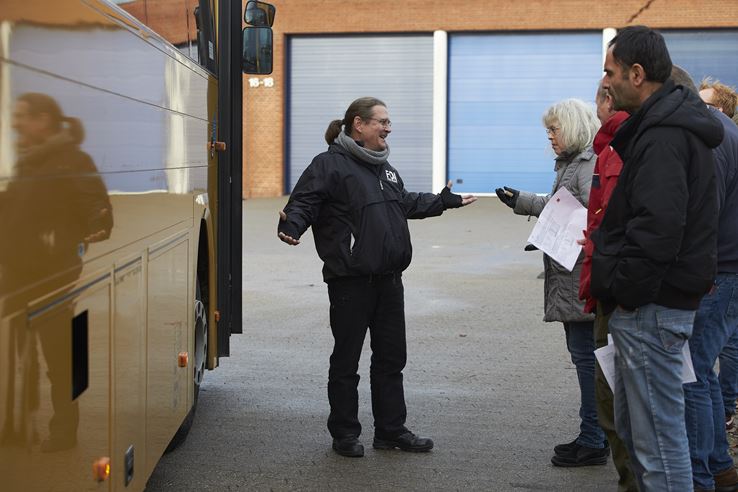 Tre mænd og en kvinde står og snakker foran indgangen til en gul bus
