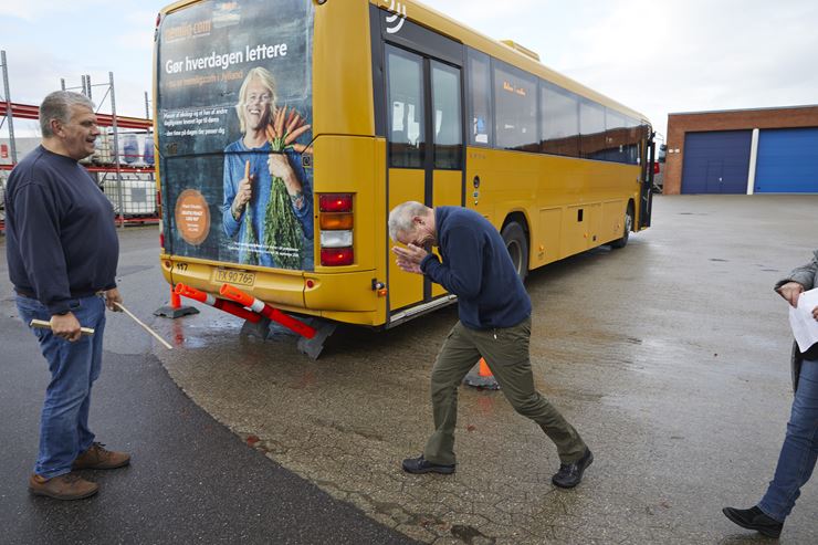 En mand holder sig for hovedet, mens han går om bag en bus som er kørt ind over to trafikkegler