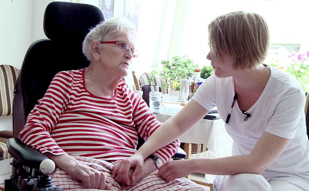 Ældre kvinde i kørestol taler med yngre kvinde i plejeuniform