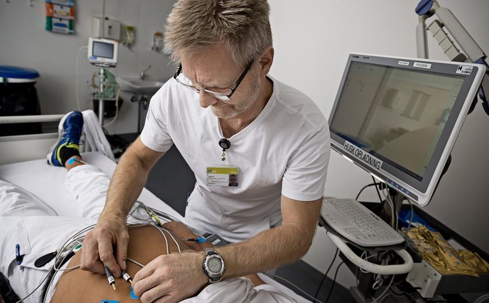Mand i hvidt hospitalstøj er ved at foretage EKG måling på en mand, der ligger i en sygeseng