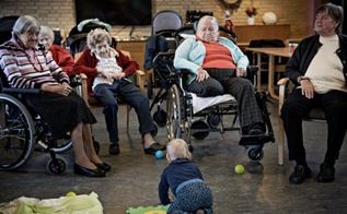 Baby spiller bold med ældre mennesker i kørestol