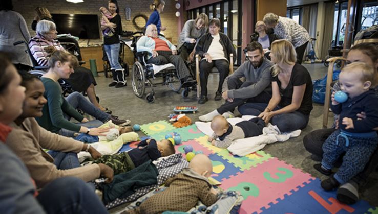 En gruppe forældre sidder i en rundkreds rundt om babyerne, der ligger på et unerlag på gulvet.