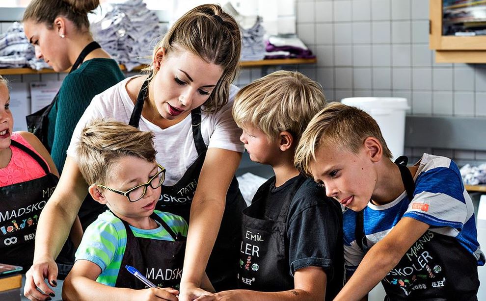 Ung kvinde underviser tre børn på en madskole