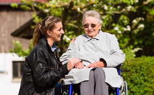 En ældrekvinde i en kørestol med en yngre kvinde ved sin side