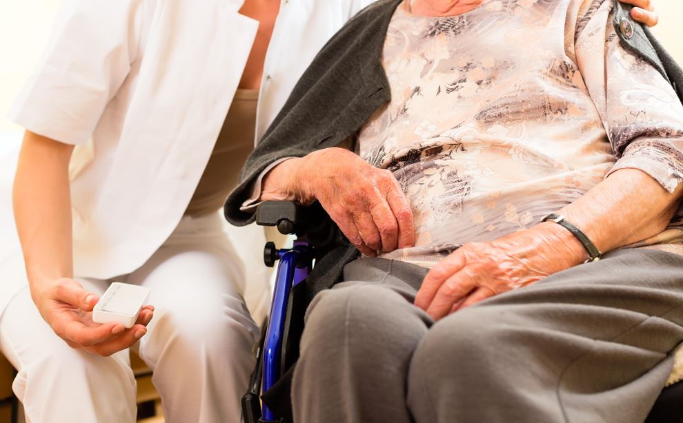 Kvinde i hvid kittel sidder ved siden af ældre kvinde i kørestol