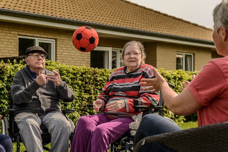 Social- og sundhedshjælper og to beboere kaster med bold på plejehjem