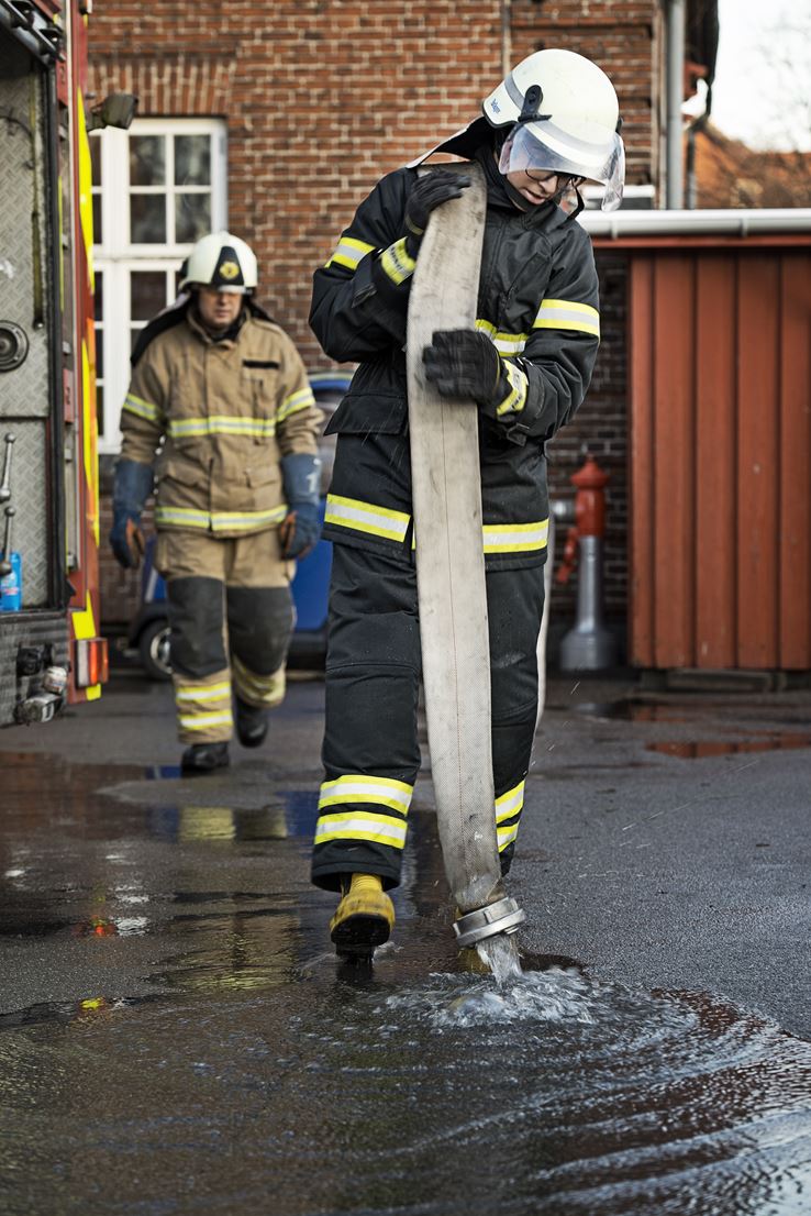 En dreng - iført branduniform - bærer på en brandslange