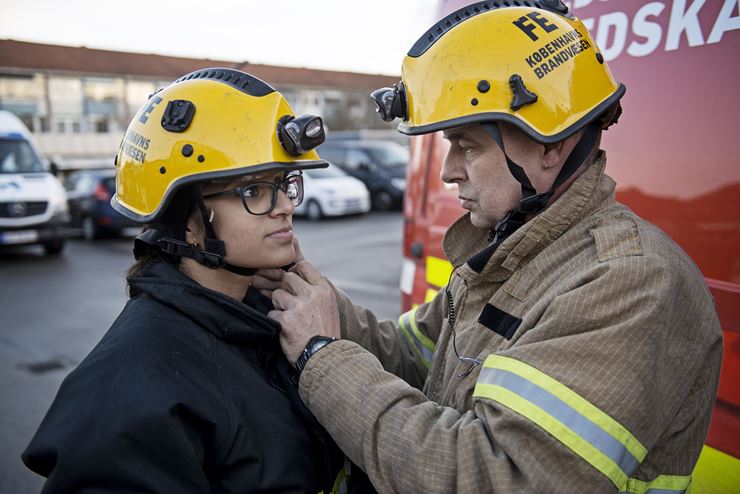 En brandmænd er i gang med at give en dreng en brandhjelm på