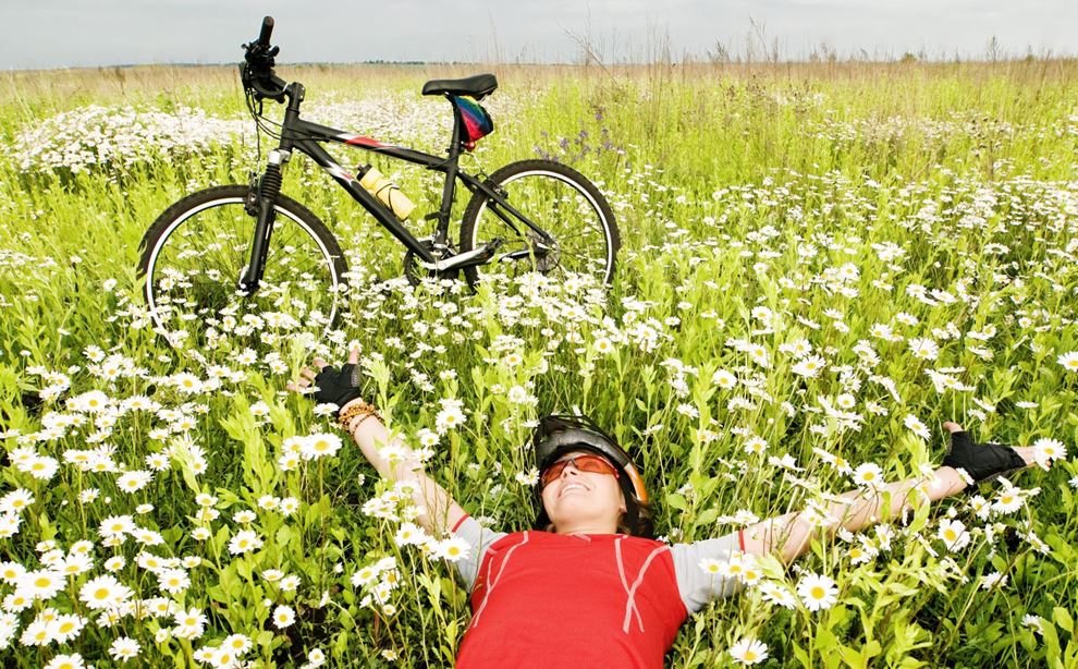 En kvinde ligger på en eng med en cykel stående ved siden af hende