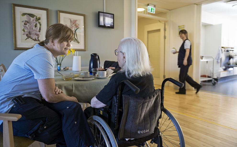 En social- og sundhedsassistent taler med en ældre borger i kørestol