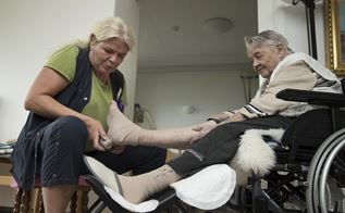 En social- og sundhedsassistent hjælper en ældre borger med strømper