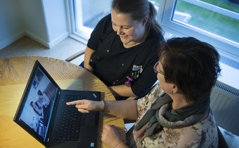 To kvinder sidder ved et bord og kigger på en bærbar computer