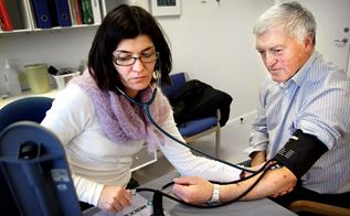 En mandlig patient får målt blodtryk af en kvindelig læge