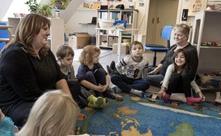 Børn og voksne sidder på gulvet i en børnehave