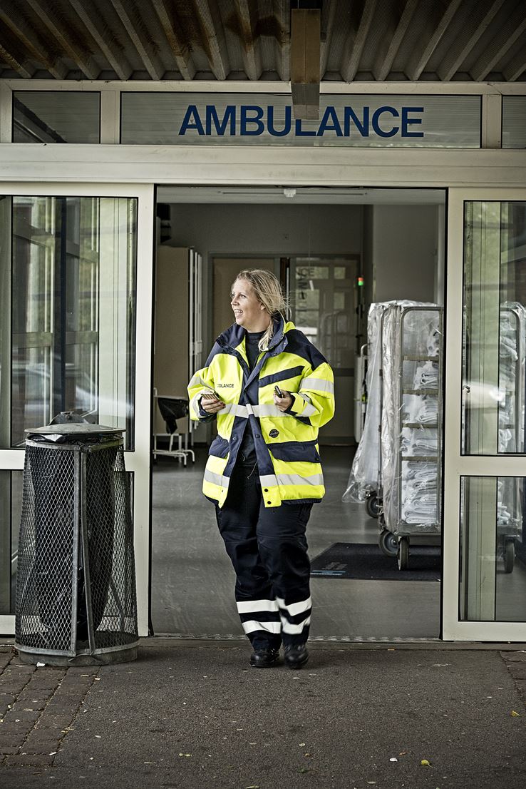En kvinde, iført gul uniform, står ved en indgang hvorpå der står ambulance