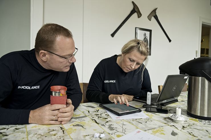 En mand og dame sidder ved et bord, hvor kvinden sidder med en computer, en tablet og nogle mobiler