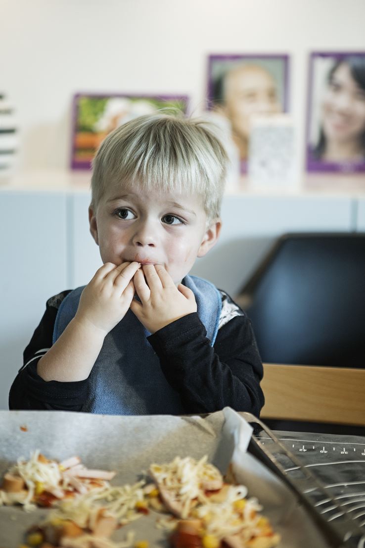 En dreng sidder med sine fingre i munden foran en bradepande