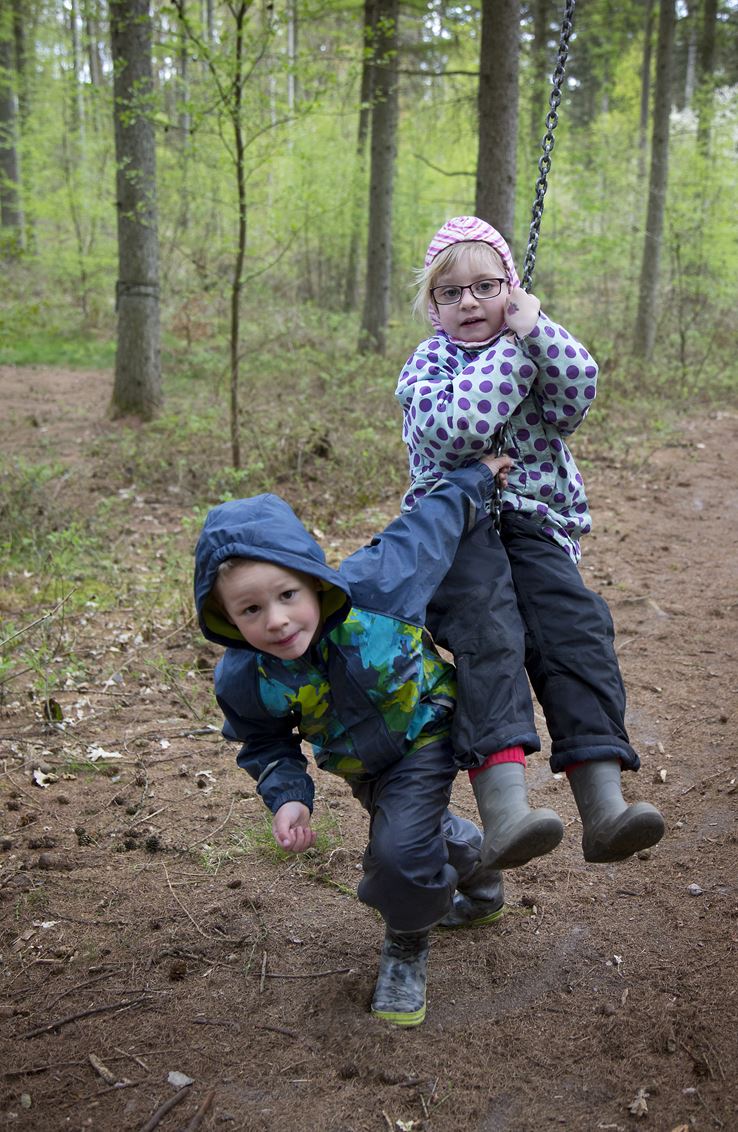 En dreng er i gang med at skubbe en pige på en gynge i en skov
