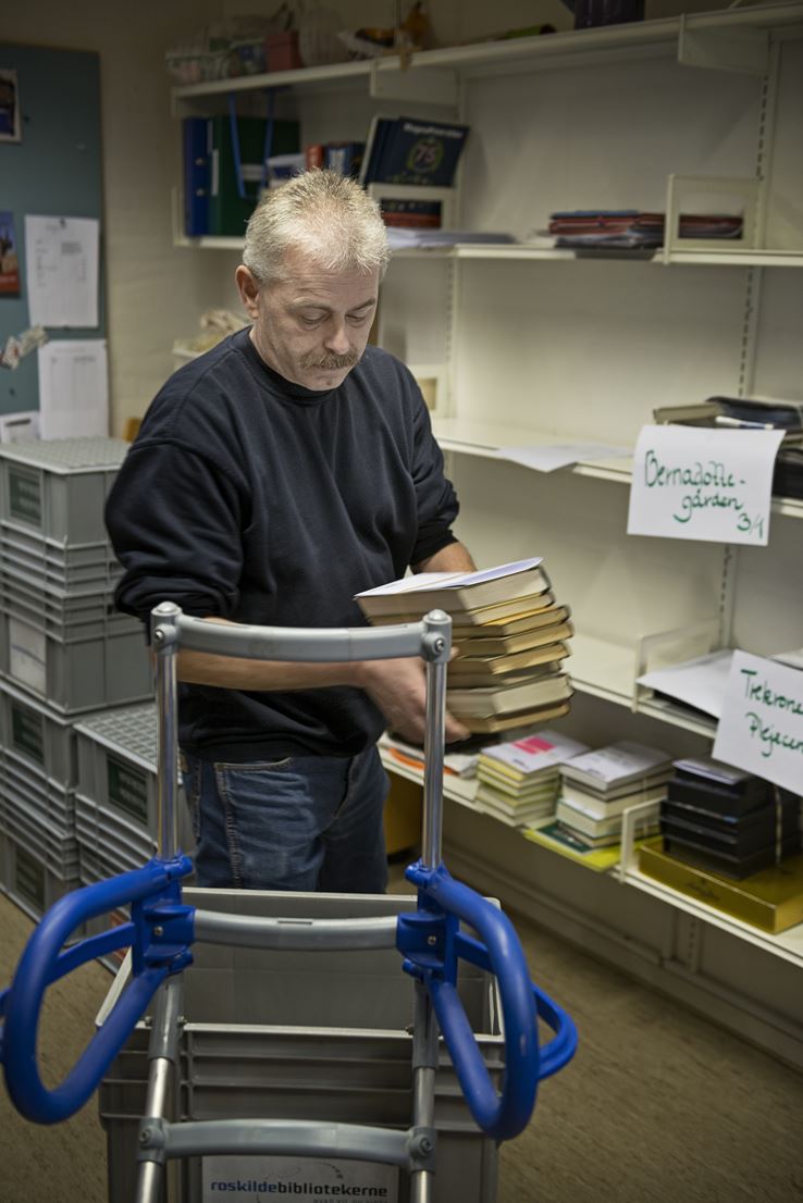 En mand står og sætter bøger på plads på nogle hylder