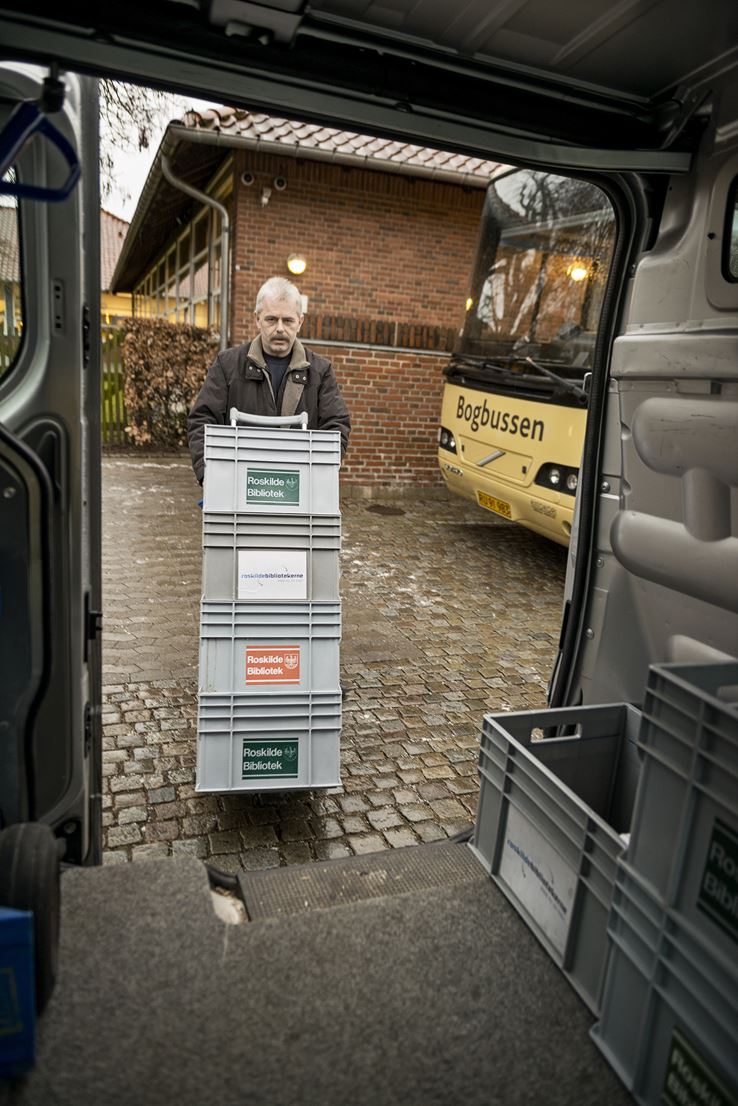 En mand er igang med at læsse en masse plastickasser ind i en varevogn