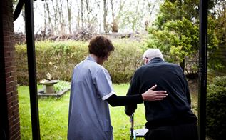 Kvindelig sosu-medarbejder hjælper ældre mand ud i haven