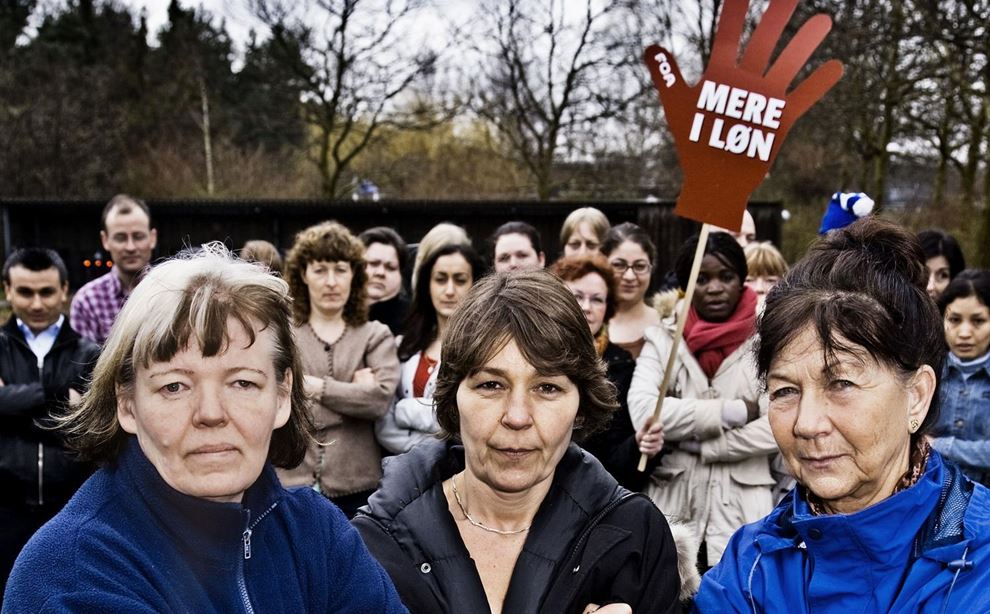 Em masse kvinder demonstrerer på en plads med skilt for højere løn 