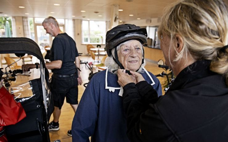sosu-assistent spænder cykelhjelm på plejehjemsbeboer