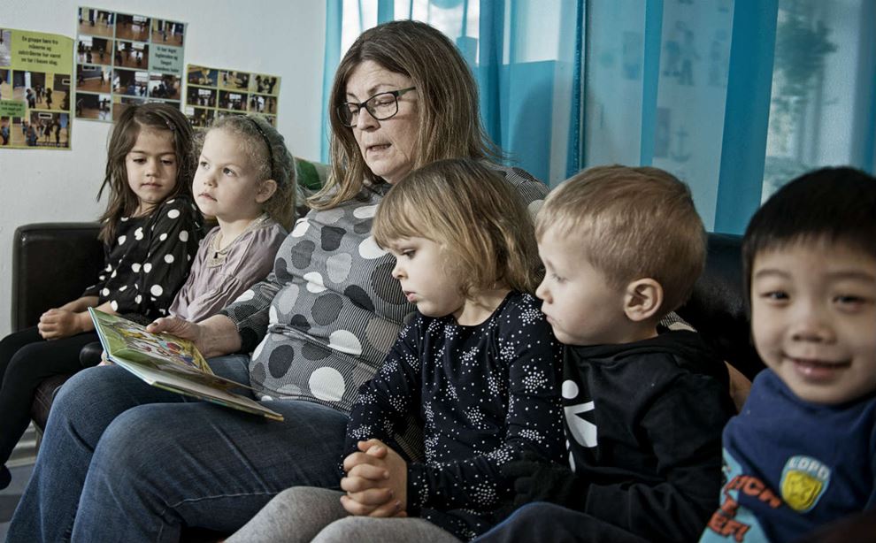 Ordblind pædagogmedhjælper læser bog for børn i sofa