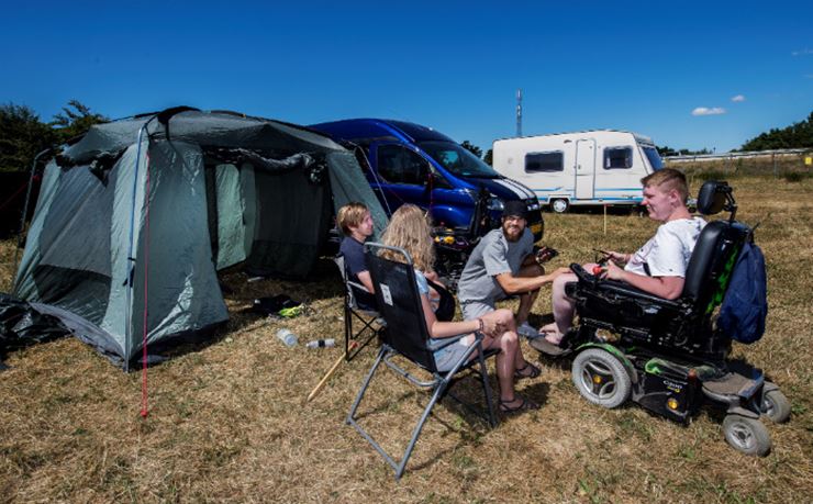 Handikappet og hjælpere sidder foran telt på Roskilde Festival