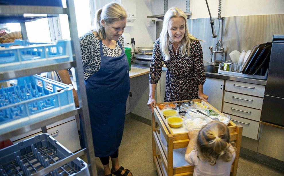 Køkkenmedhjælper og pædagog hjælper barn med rullebord