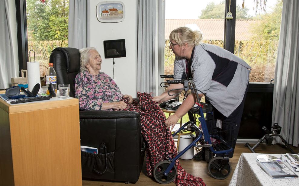 Ældre dame sidder i stol, mens social- og sundhedsassistent retter hendes tæppe. Foto: Heidi Lundsgaard