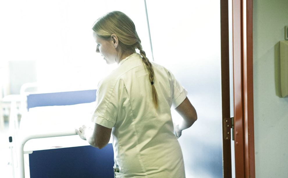 En kvinde i hvid kittel går bagved en hospitalsseng